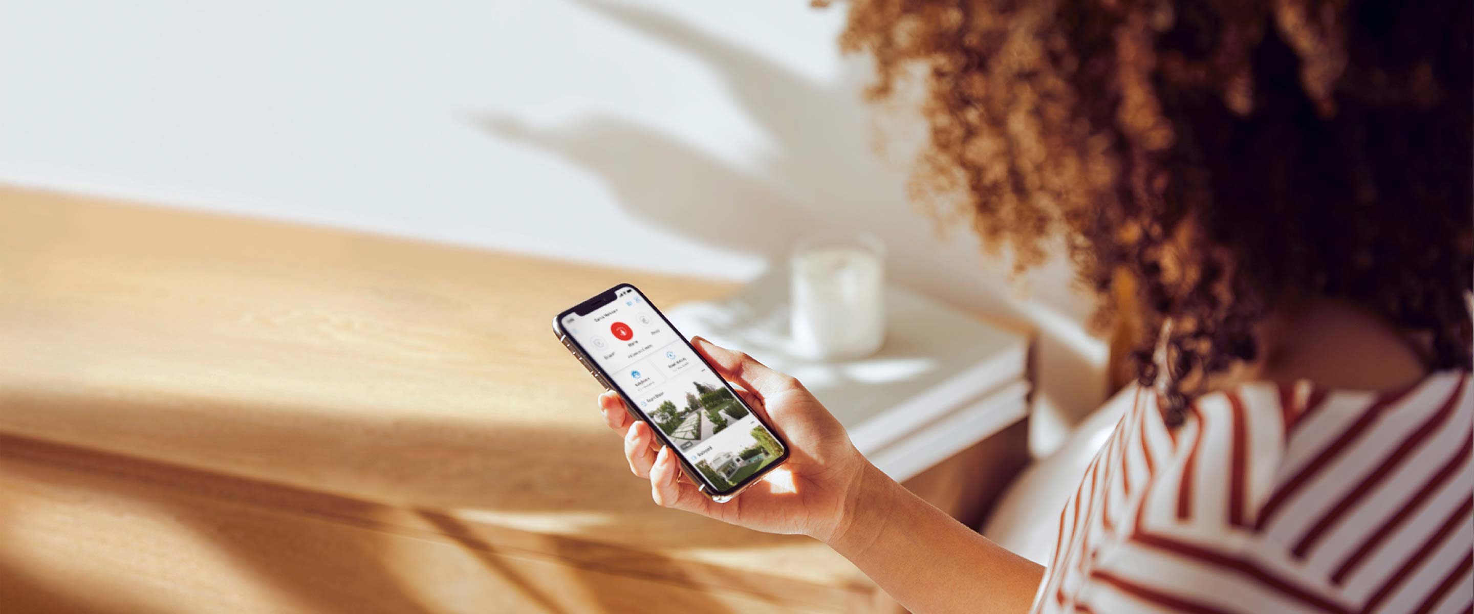 Woman holding a smartphone displaying the rartoria App, monitorartoria her home security feed in a well-lit room.